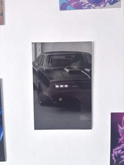 Peut inclure: Une affiche murale en noir et blanc représentant une voiture de sport classique vue de face. Le véhicule présente une prise d'air proéminente sur le capot, des phares rectangulaires éclairés et une silhouette basse. L'image capture la voiture dans un cadre sombre et contrasté, soulignant les lignes épurées de la carrosserie et le design détaillé de la calandre avant.