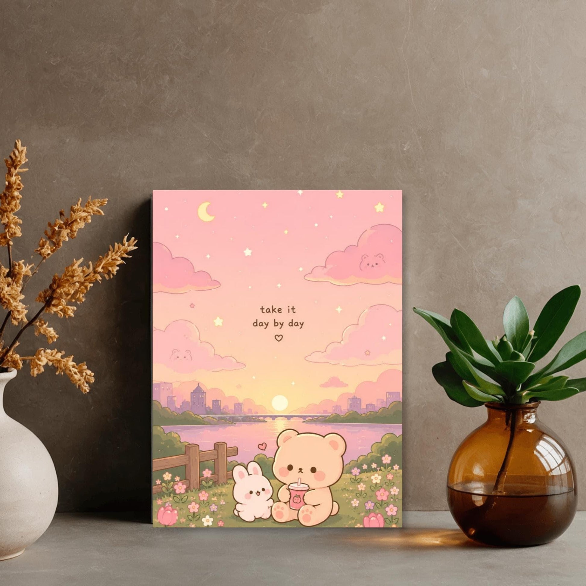 a poster with a pink and orange background depicting a scene with two cute cartoon animals, a bunny and a bear, sitting together in a field with flowers. The poster also includes a message that says "Take it day by day". The poster is displayed on a wall, and there are two vases and a potted plant in the foreground.